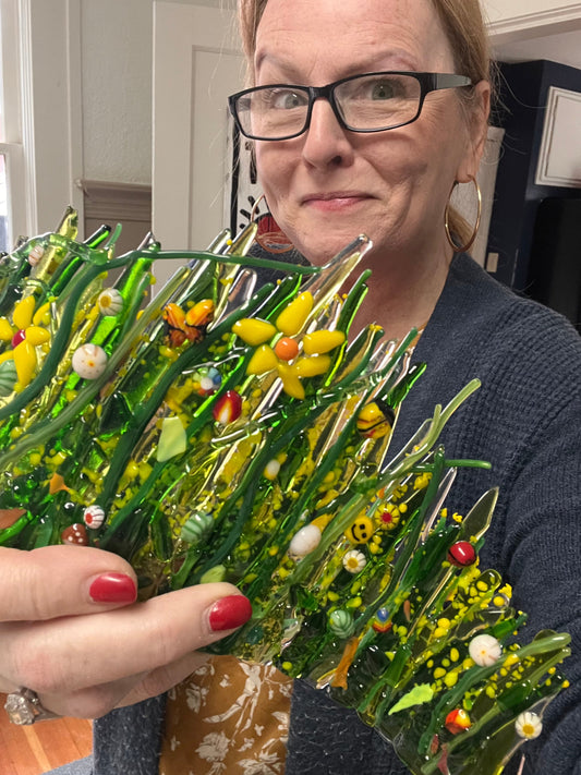 Photo of Michelle Frost holding a green fused glass garden piece with yellow flowers and colourful stringers